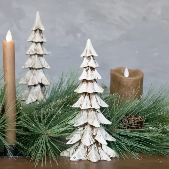 A weathered white decorative Christmas tree with layered branches, displayed among pine greenery and candles on a wooden surface.